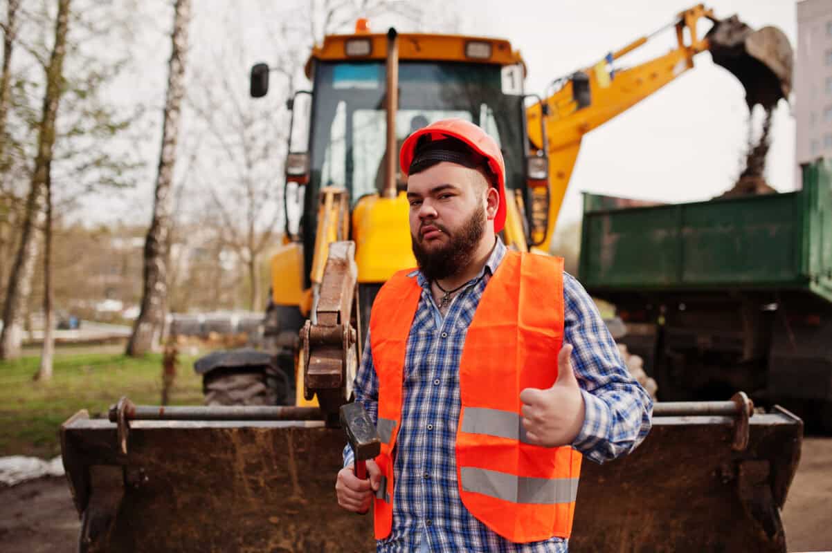 A construction worker with a hammer in one hand and making a thumbs up.